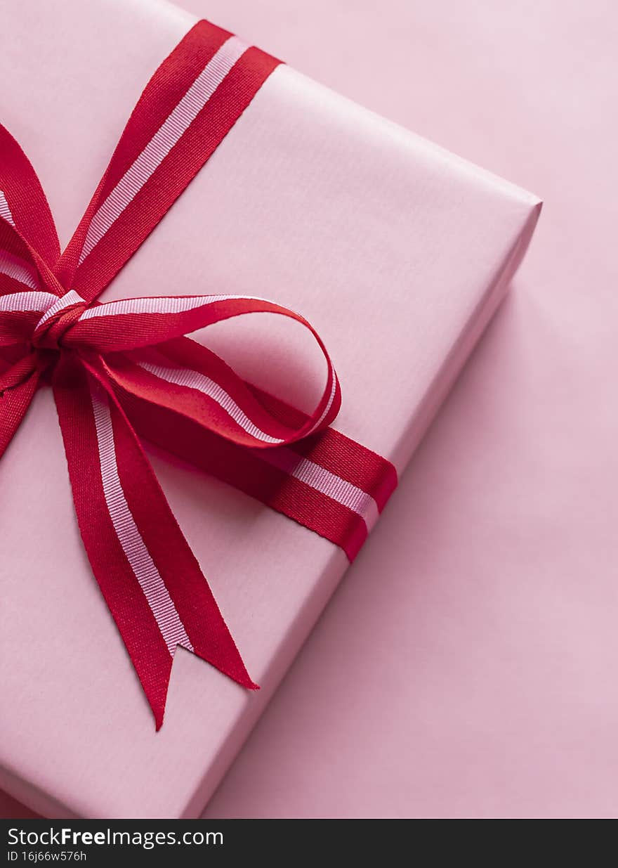 Valentine`s day celebration gift box with red bow on the pink background. Close up