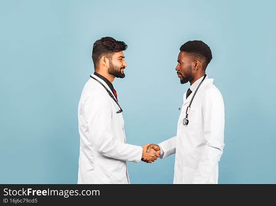 Portrait of smiling medical worker in white lab coat with stethoscope conferring with young doctor on blue background. Portrait of smiling medical worker in white lab coat with stethoscope conferring with young doctor on blue background