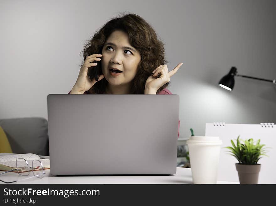 Asian businesswoman work at home with laptop and talking on smartphone and smiling. Female working on computer and using cell mobi