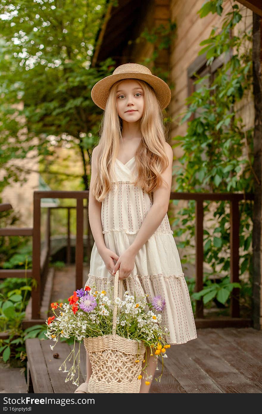 Portrait of happy tween girl in summer sundress and straw hat enjoying vacation in country estate, standing on doorstep of house with wicker basket of colorful wildflowers. Portrait of happy tween girl in summer sundress and straw hat enjoying vacation in country estate, standing on doorstep of house with wicker basket of colorful wildflowers