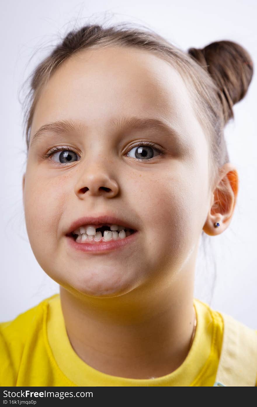 Charming little female kid face with opened mouth showing missing front baby tooth in yellow t-shirt on white background. First teeth changing. Going to dentist to do tooth treatment.