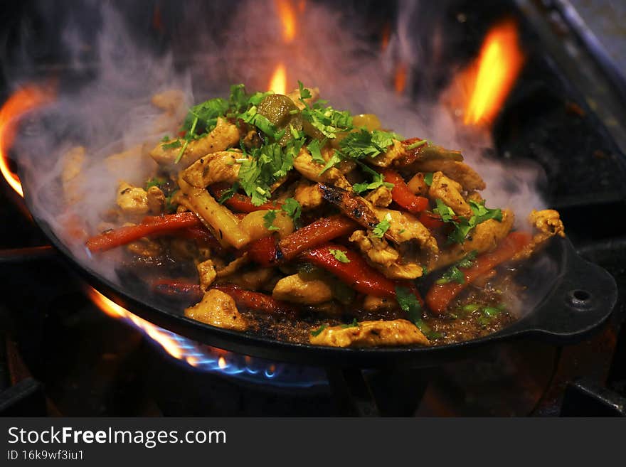 Mexican food, chicken fajitas preparing on a hot smoking sizzling plate.