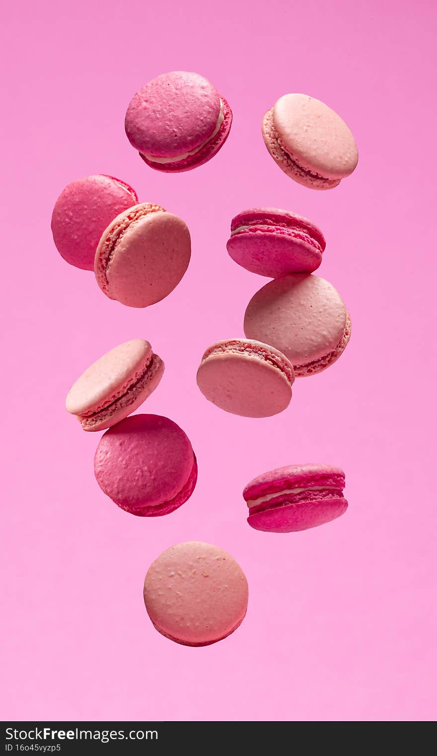 Colorful sweet macarons or macaroons, flavored cookies floating in the air on pink background.