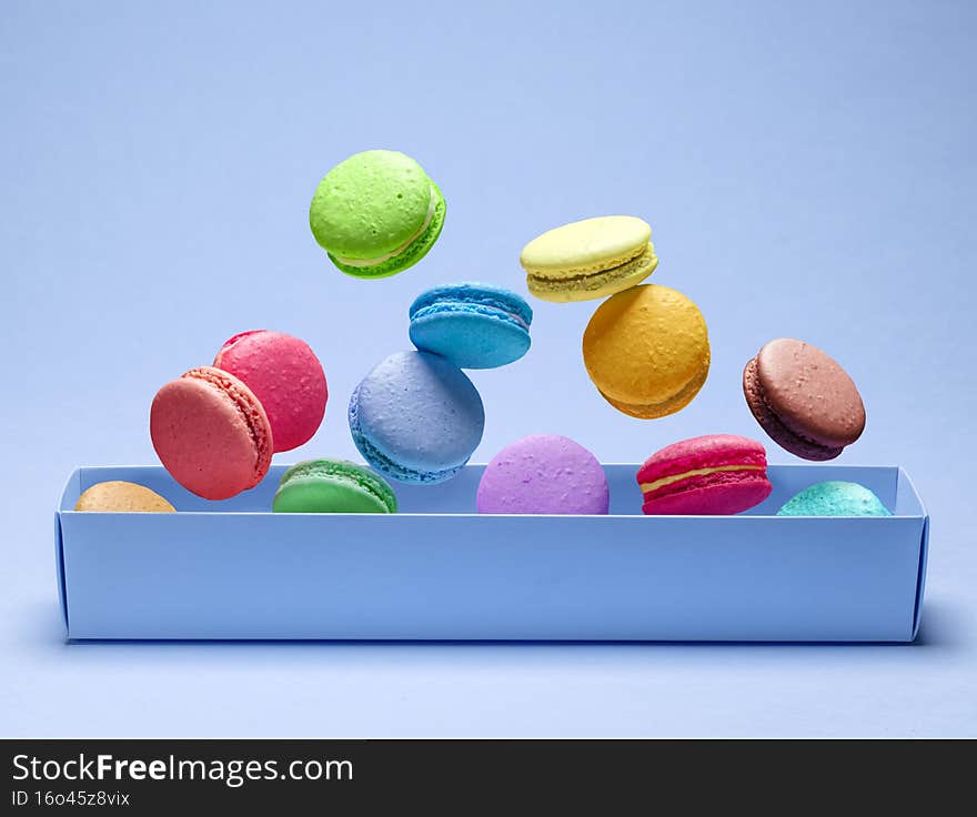 Colorful sweet macarons or macaroons, flavored cookies floating in the air above the paper box. Blue background.