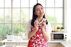 Happy Smiling Beautiful Young Asian Woman In Cute Red Heart Apron, Standing Behind Kitchen Counter, Holding Valentine Homemade Stock Photo