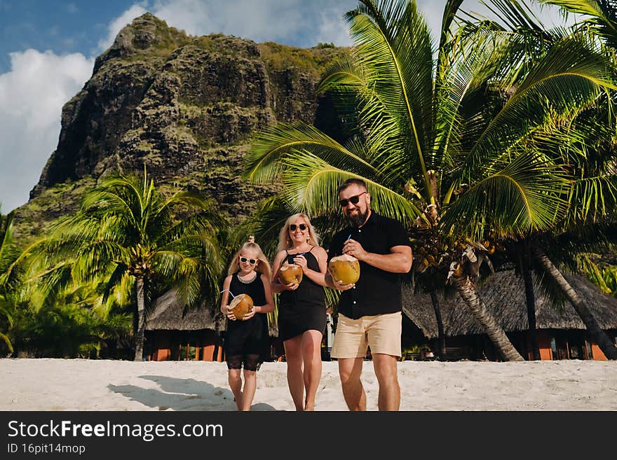 a stylish family in black clothes with coconuts in their hands on the beach of the island of Mauritius.Beautiful family on the island of Mauritius in the Indian ocean.