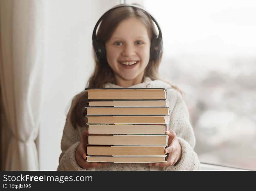 Distance learning with books. Audiobook concept: girl with headphones and books in hands