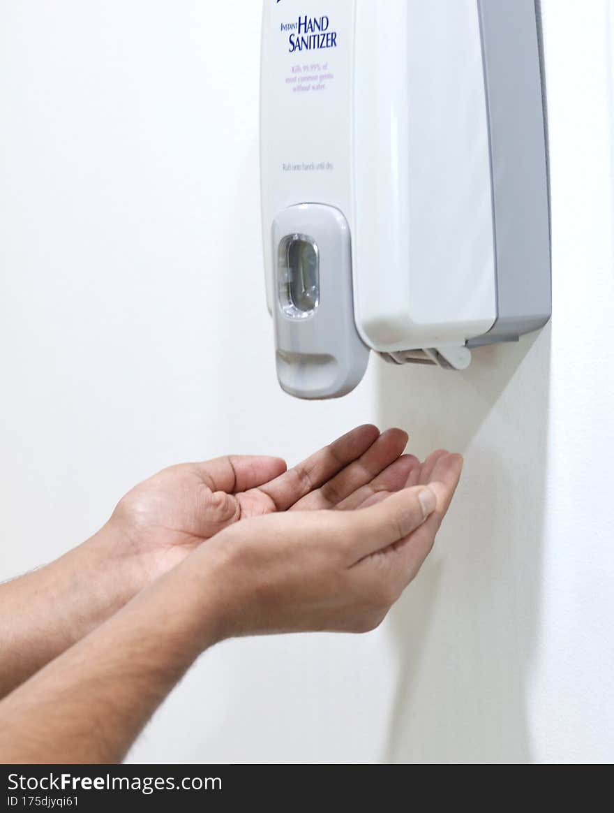 Hands placed under an automatic wall mounted sanitiser dispenser.