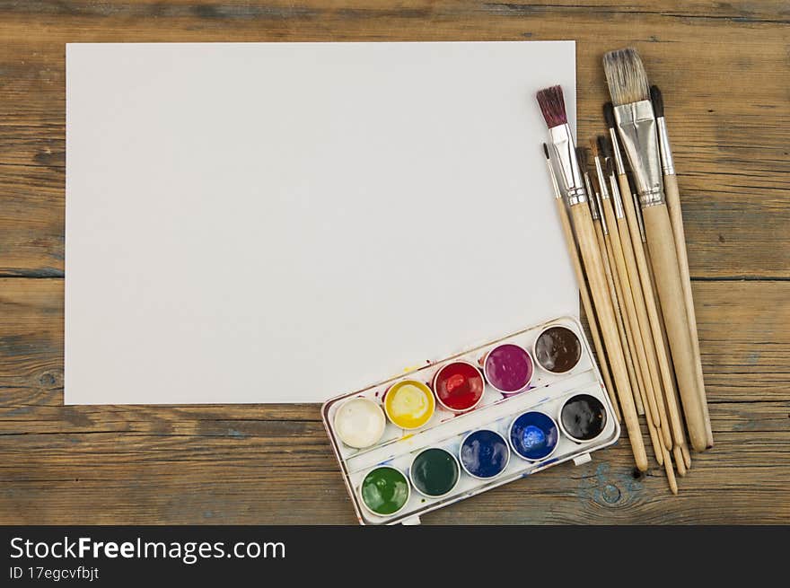 A paint brushes on old wooden background with blank white paper