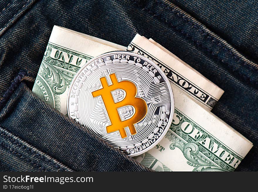 A silver physical Bitcoin coin with golden symbol B and folded American dollars sticks out of the pocket of blue jeans close-up. Saving money in cryptocurrency concept. Business background. A silver physical Bitcoin coin with golden symbol B and folded American dollars sticks out of the pocket of blue jeans close-up. Saving money in cryptocurrency concept. Business background.