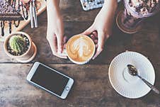 Top View Of Female Hands Holding A Cup Of Hot Milk Coffee On The Wooden Table In Coffee Shop. Stock Photos