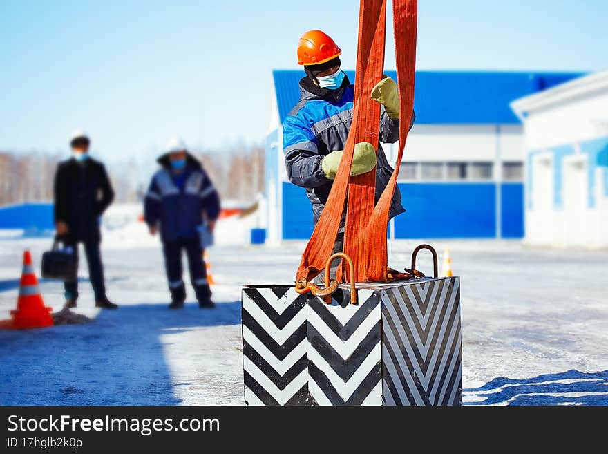 Working slinger passes exam on lifting loads. Real scene. Commission evaluates skill of slinger. Worker in helmet on street on winter day.