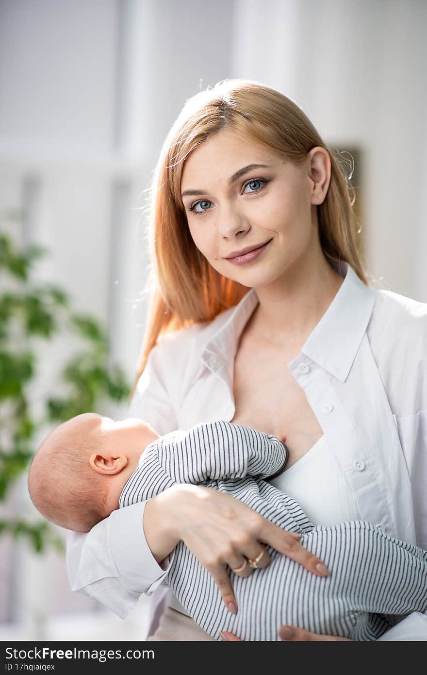 Mom holds the baby in her arms and looks at the camera. Behind them is a beautiful large green flowerpot. Beautiful portrait photo of mom and baby.