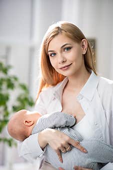 Mom Holds The Baby In Her Arms And Looks At The Camera. Behind Them Is A Beautiful Large Green Flowerpot. Stock Image