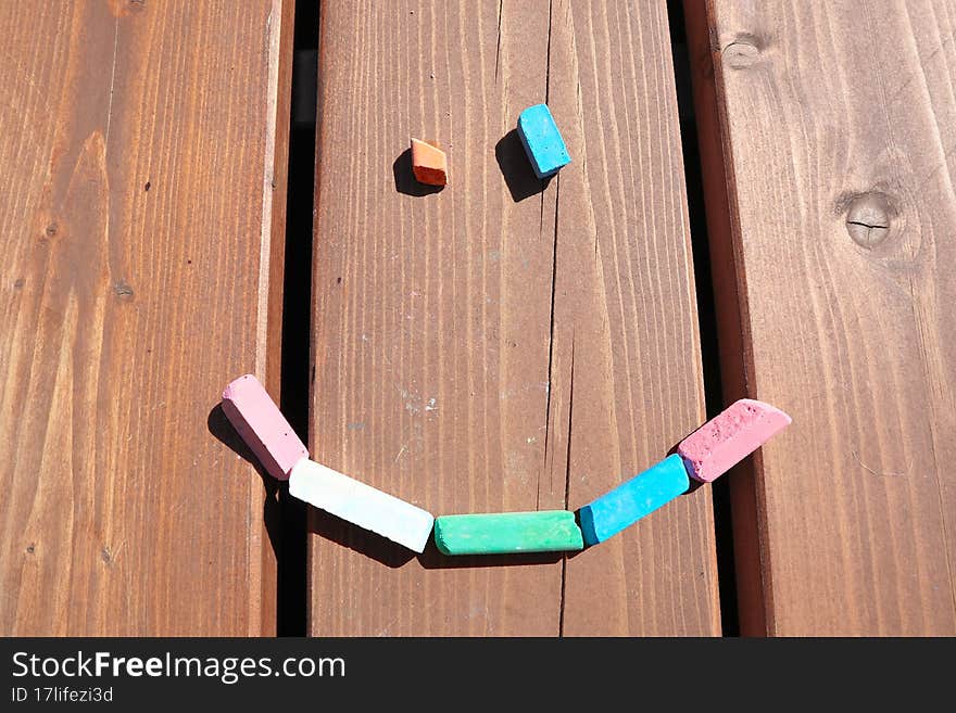 a face made of crayons on a wooden background. happy summer