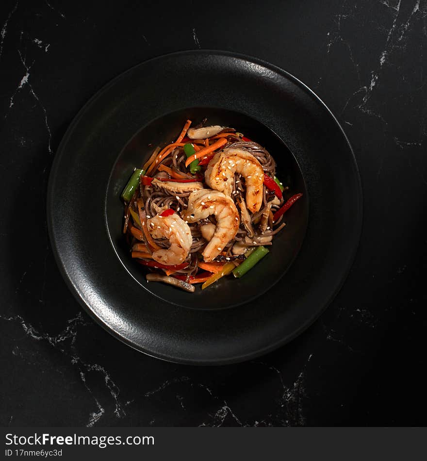 Funchoza with shrimp and vegetables on a black background, copy space. Buckwheat noodles on a dark stone background. Asian cuisine, Wok menu. Traditional Asian food, Top view. Funchoza with shrimp and vegetables on a black background, copy space. Buckwheat noodles on a dark stone background. Asian cuisine, Wok menu. Traditional Asian food, Top view