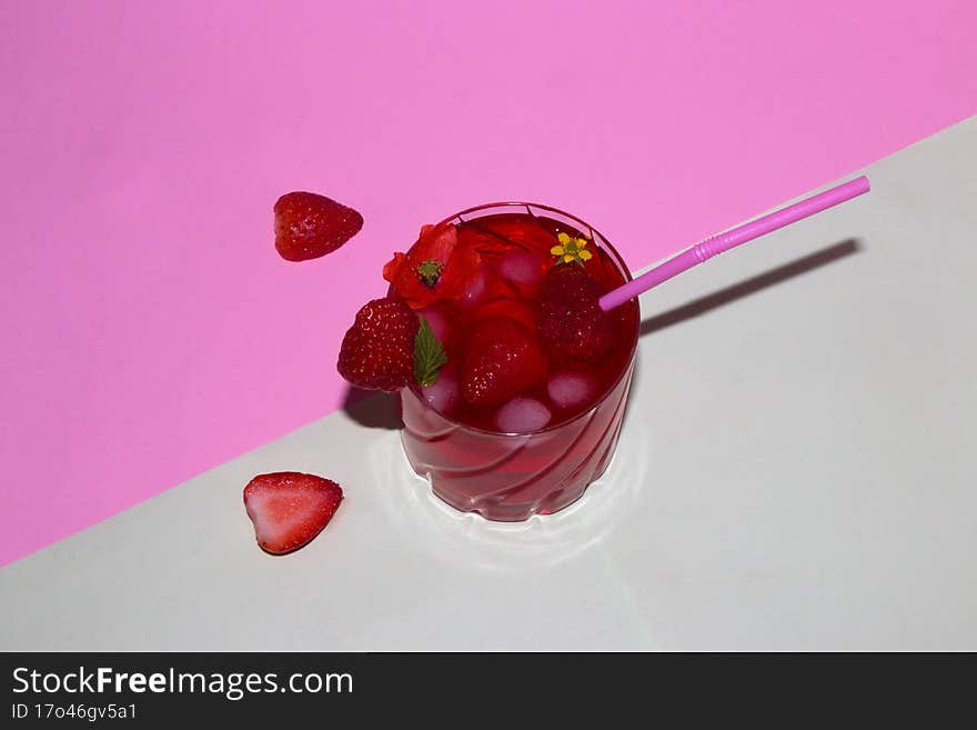 a glass of strawberry juice arranged with flowers and strawberries, next to a glass of strawberries cut in half on a pastel pink-g