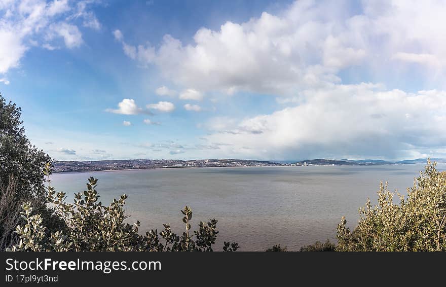 View from Mumbles hill over Swansea Bay, with cloudy blue sky and the tide is in.