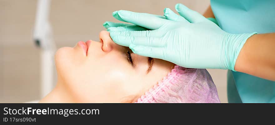 Cosmetologist with gloved hands applies a moisturizing mask with peeling cream on the female face. Facial cosmetology treatment. Procedures for facial care