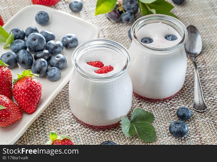 Two glass containers with plain yoghurt and berries on the table.   Light summer mood.