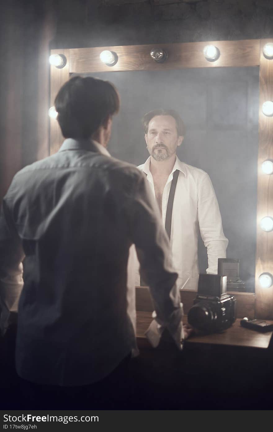 Man in white shirt in front of mirrow looking at own reflection in lights. Man in white shirt in front of mirrow looking at own reflection in lights