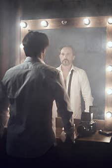 Man In White Unbuttoned Shirt With Balck Tie In Front Of Mirrow With Lights Looking At Own Reflection Stock Photos
