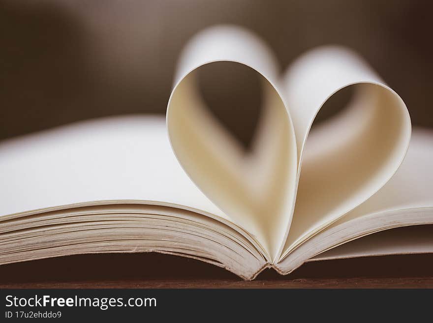 Close up heart shape from paper book on wooden table with vintage blur background