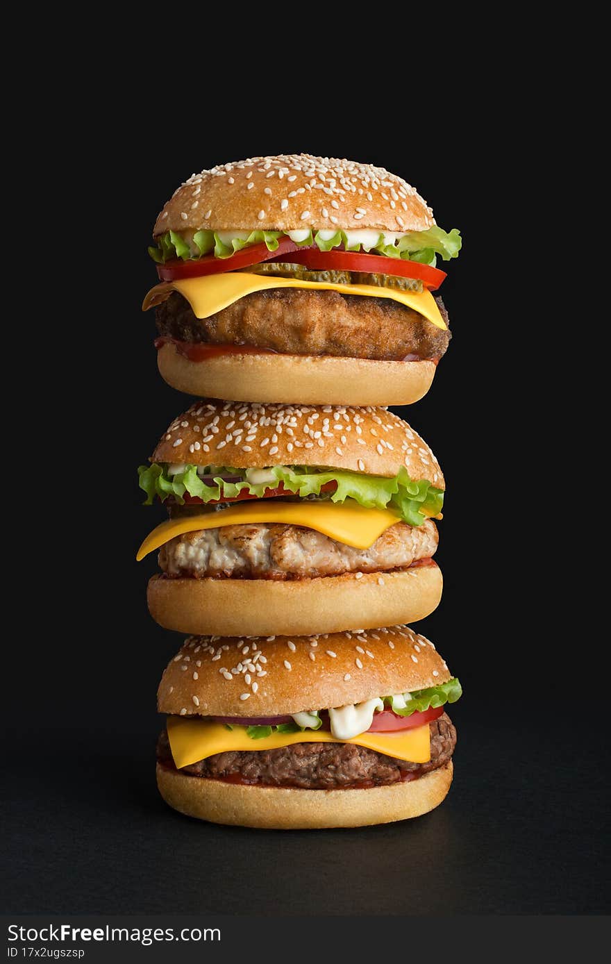 stack of three different burgers on black background