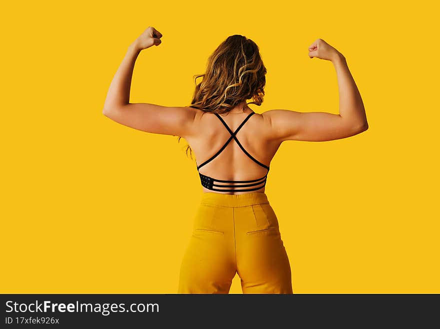 young beautiful woman in yellow sport clothes showing biceps arm muscle posing on a yellow background
