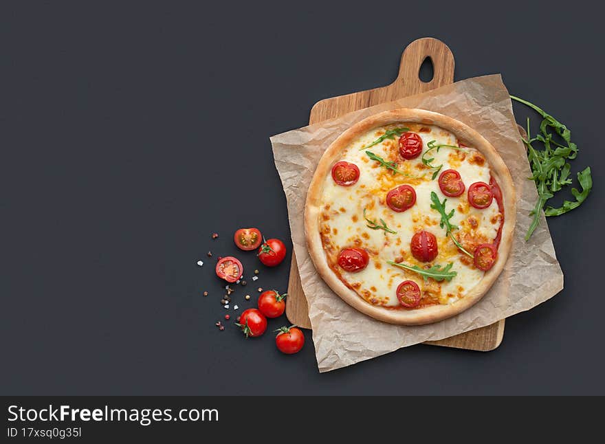 margarita pizza on a board with ingredients on a black background