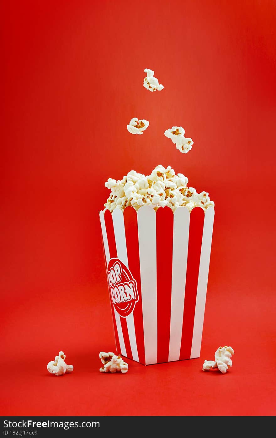 Falling popcorn in a striped cardboard box on a red background, vertical view. Popcorn levitation. Cinema time