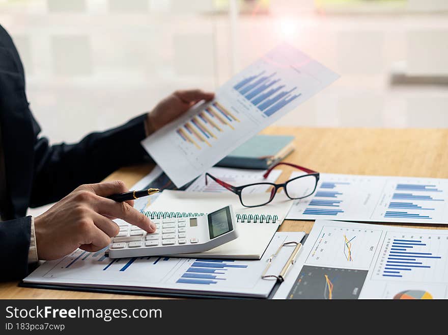 At the accounting desk, an accountant presses a calculator to analyze investment charts to generate monthly financial reports or company profits...
