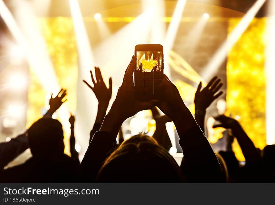 The fan holding his smart mobile phone and photographing a rock concert.