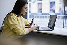 Concentrated Brunette Female Blogger Watching Vlog On Website Sitting With Devices In Cafe Interior Stock Photo