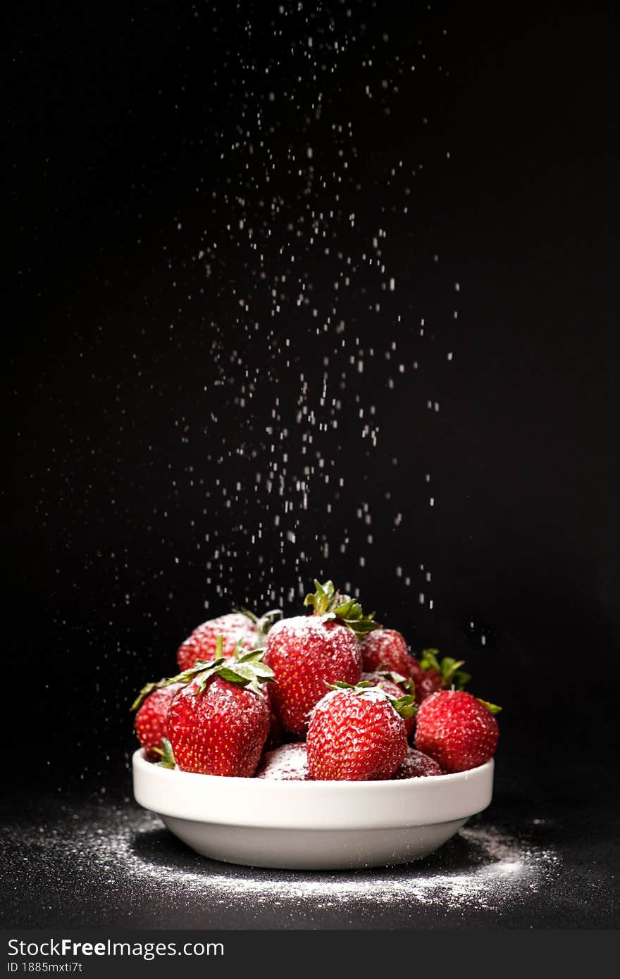 Powdered sugar falls on strawberries in a plate on a black background.