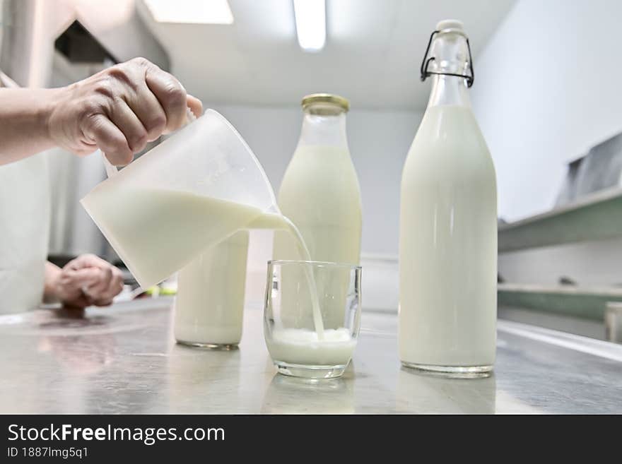 Pouring milk from a jug into a glass. In the background full glass bottles.