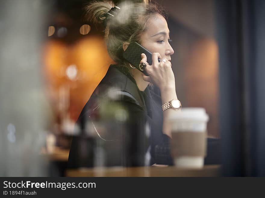 Asian woman talking chatting conversing using cellphone in coffee shop. Asian woman talking chatting conversing using cellphone in coffee shop