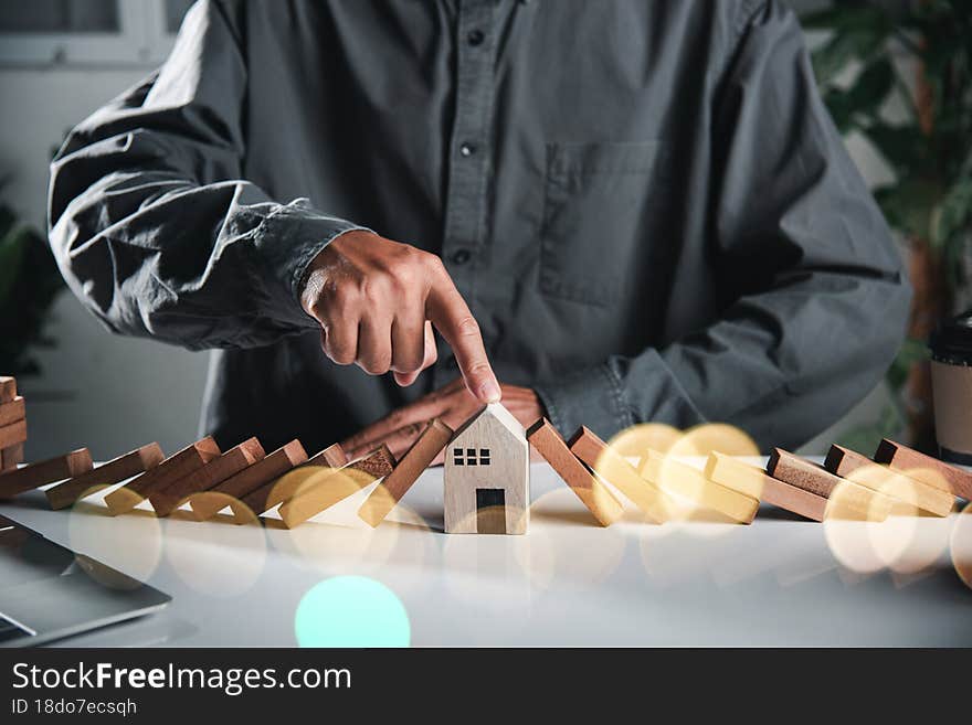 Business risk plan real estate protection. Man hand blocks wood block from many row falling wooden block like domino to house model, Insurance ideas to prevent loss concept