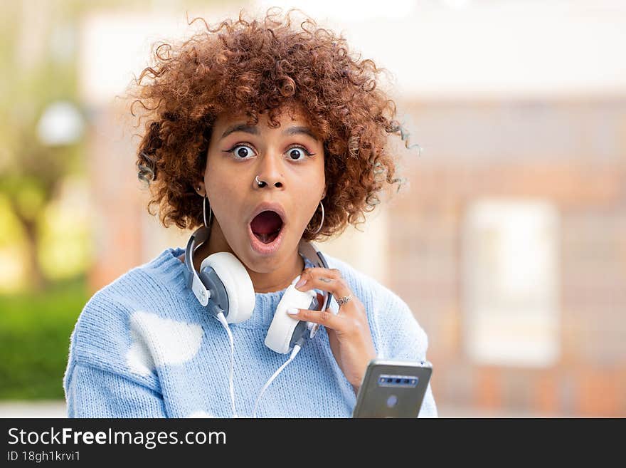 Girl with mobile phone and expression of surprise outdoors