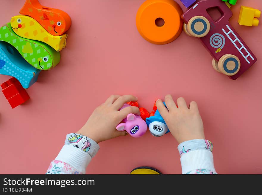 Child is playing with colorful wooden and plastic toys, on pink background indoors