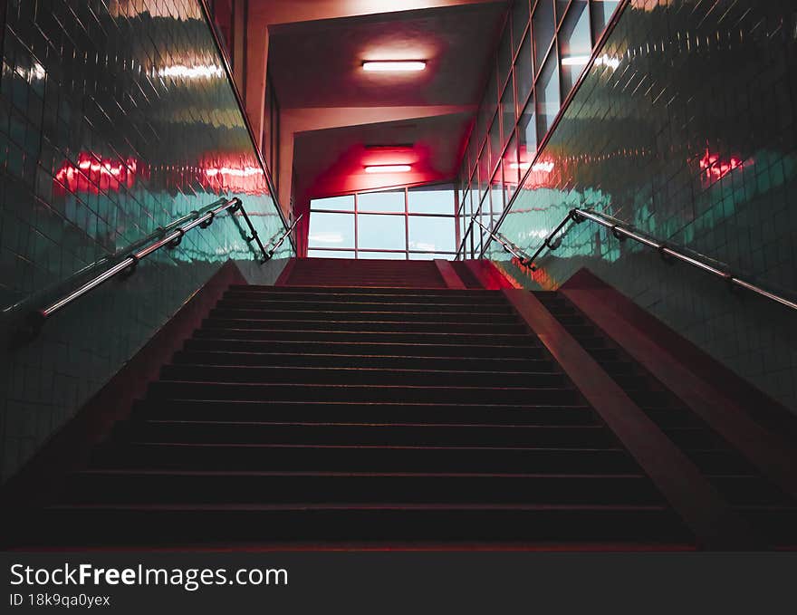 Urban colored building, art, modern steps lead up the stairs to the building window. Steps in a building with turquoise walls and red lights on the ceiling lead up the stairs to the window