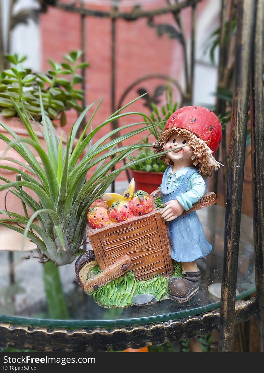 A gardening decorative figure, a little girl pushes a wheelbarrow next to a plant