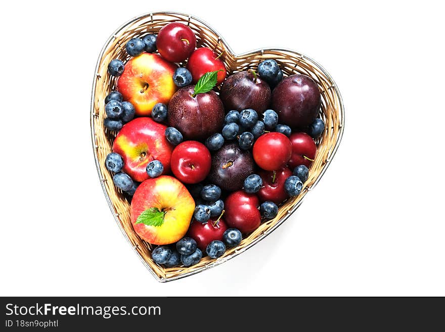 Fruit for the Jewish New Year. Red apples and plums in straw basket made in the shape of heart on white background. Copy space