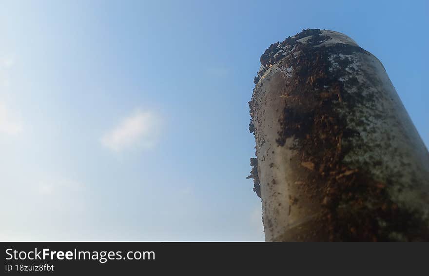 a bottle made of glass, looks very dirty, soaring into the blue sky with white clouds.