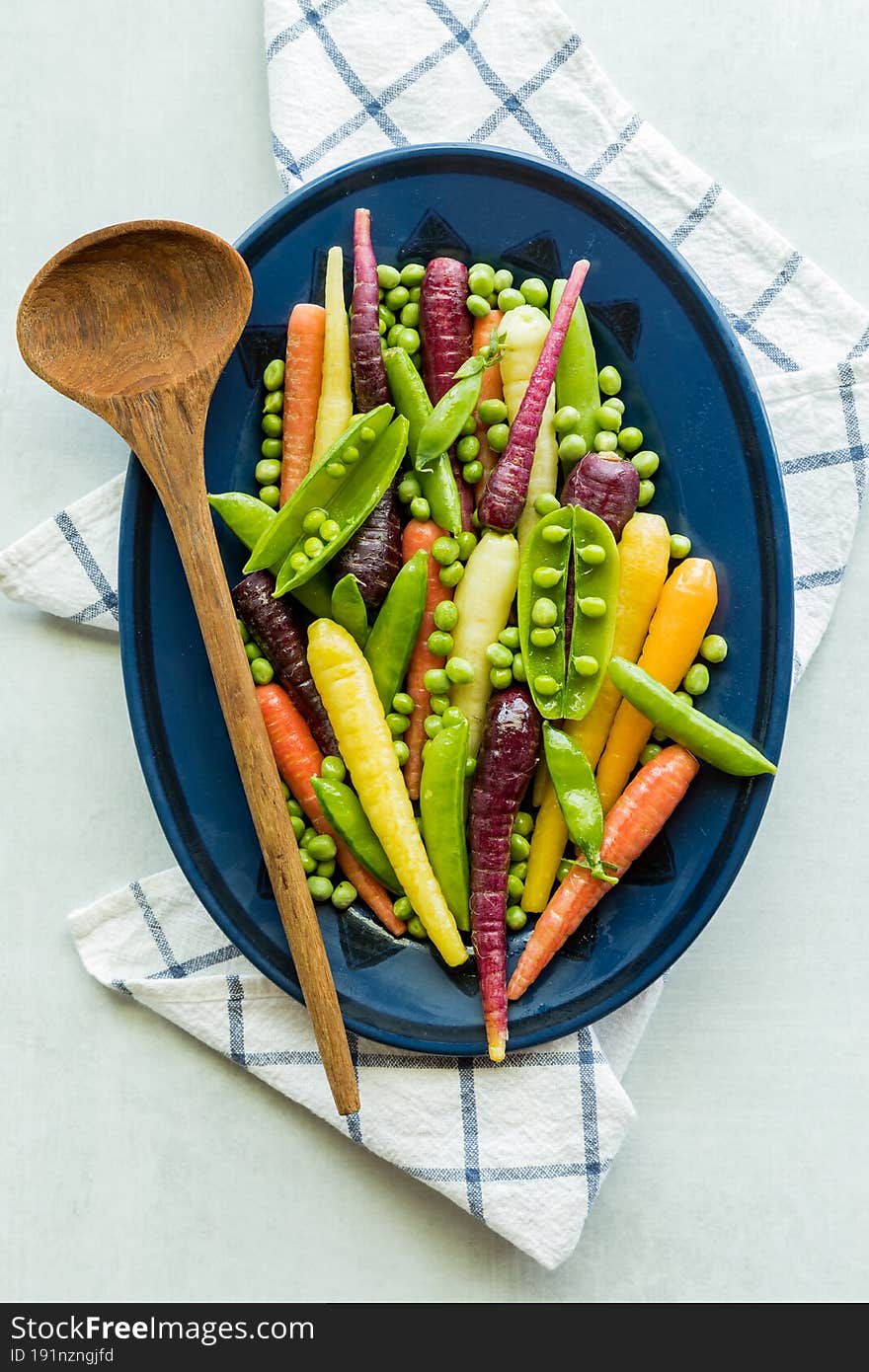 A medley of pea pods, peas and rainbow carrots on an oval plate.