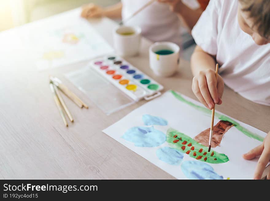 Children paint green grass with a tree and blue clouds.