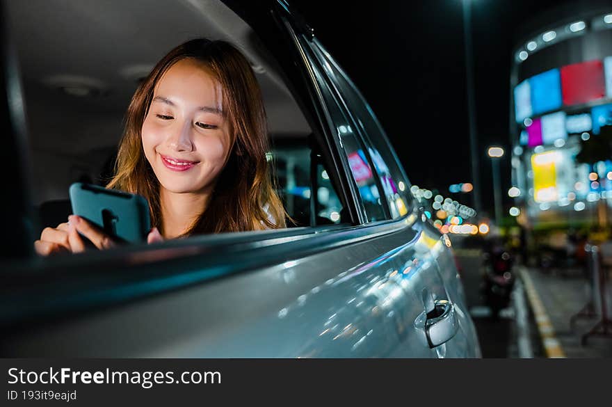 Happy beautiful woman texting smartphone sitting back seat her car in urban, Asian businesswoman commuting from office in Taxi backseat with mobile phone on road in city at night after late work