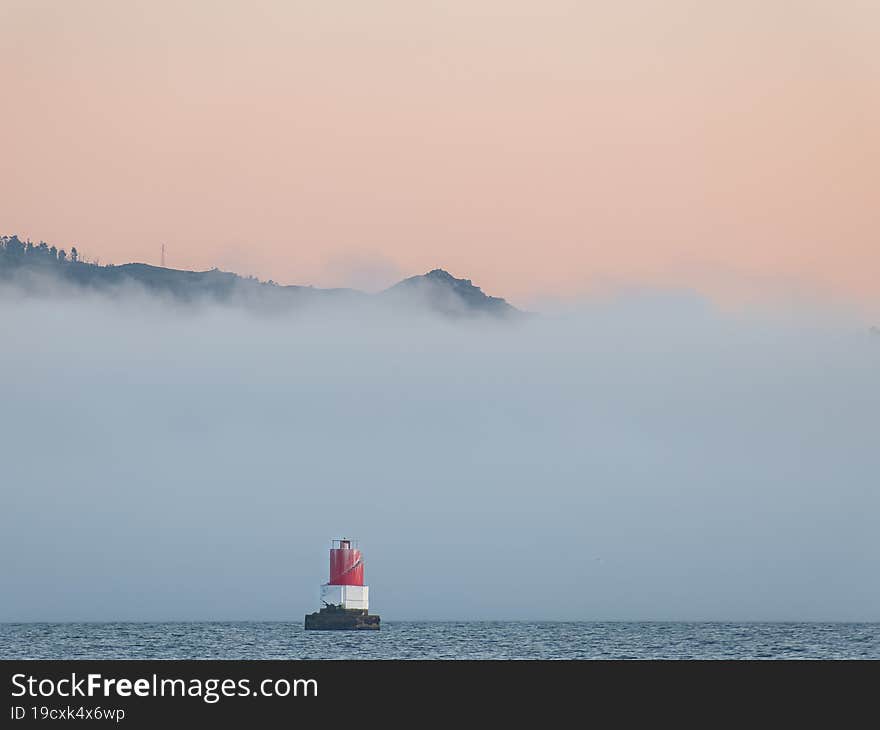 Seascape with lighthouse in the sea next to a fog bank in summer