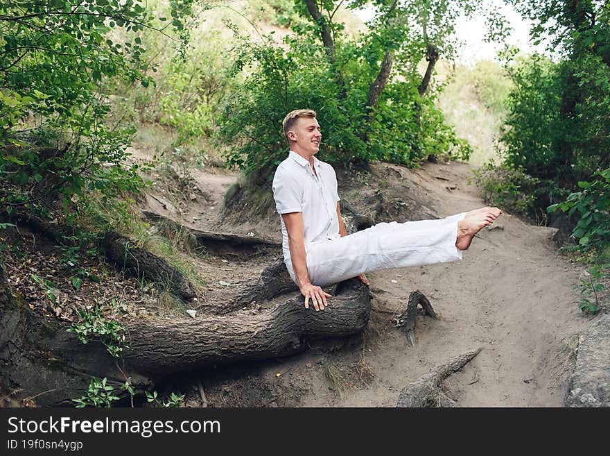 A young man practices yoga and performs a corner stand on the roots of an old tree.