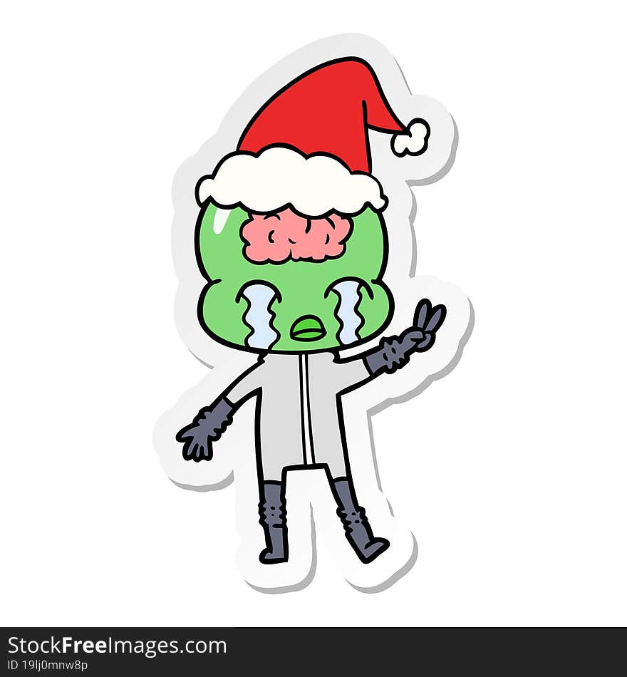 hand drawn sticker cartoon of a big brain alien crying and giving peace sign wearing santa hat